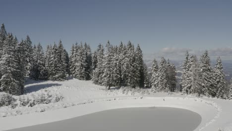 Rain-water-catchment-lake-at-Kope-ski-resort-in-Slovenia-during-winter,-Aerial-orbit-around-shot