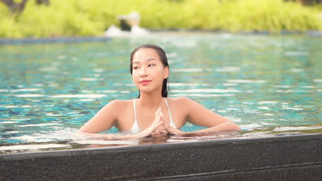 Hermosa-Mujer-Asiática-En-El-Borde-De-La-Piscina-Disfrutando-Del-Buen-Tiempo-Y-El-Agua-En-Vacaciones-Tropicales-Exóticas,-Cámara-Lenta