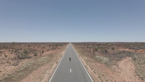 Dama-Camina-A-Través-De-La-Soleada-Carretera-Rural-En-Un-Desolado-Desierto-árido-En-El-Interior-De-Australia,-Territorio-Del-Norte