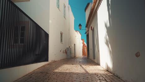 Portugal-Algarve-Loule-empty-narrow-stone-street-with-trees-shade,-public-lantern-at-morning-sunshine-4K