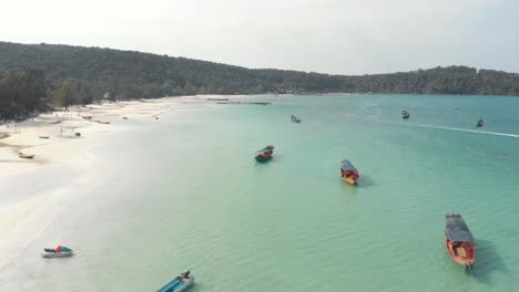 Shoreline-circling-around-shallow-bay-with-fisher-boats-moored-in-Saracen-Bay-in-Koh-Rong-Sanloem,-Cambodia---Aerial-Panoramic-shot