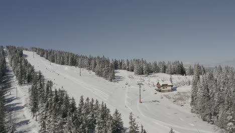 Skiers-going-downhill-on-Kope-ski-resort-Ribnica-One-track-in-Slovenia,-Aerial-dolly-left-shot