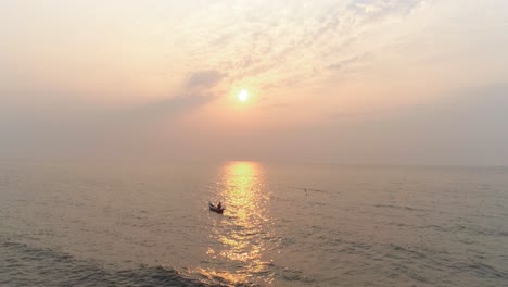 A-fisherman-in-a-boat-with-the-sun-setting-in-the-back-capture-with-a-drone-in-the-Arabian-sea-from-the-coast-of-Mumbai,-where-the-next-coastal-road-project-will-be-coming-up
