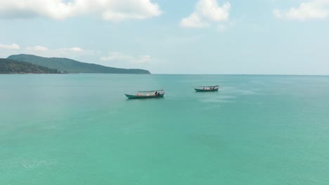 Fishing-boats-moored-and-resting-above-beautiful-clear-blue-water-at-Saracen-Bay-in-Koh-Rong-Sanloem,-Cambodia---Aerial-Low-angle-Orbit-shot