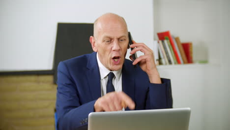 An-angry-mature-businessman-is-talking-on-the-phone-in-his-home-office