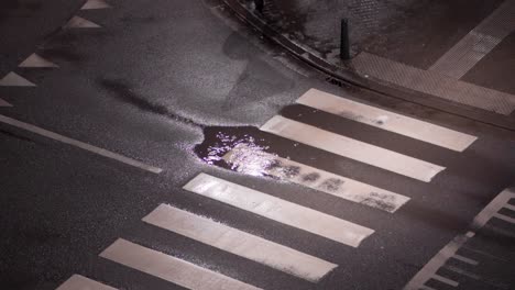High-angle-shot-of-raindrops-in-a-puddle-on-the-pedestrian-crossing-in-the-city-street-at-night