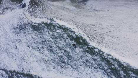 Two-hikers-standing-on-a-snowy-ridge-in-the-Peak-District,-aerial-view