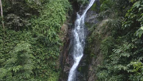 Pan-up-shot,-lush-jungle-waterfall-with-tropical-vegetation-surrounding