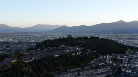 Lijiang-city-background-landscape-at-sunset,-aerial-view-over-city-and-mountains