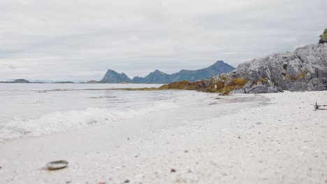 Ruhige-Wellen-Durch-Weißen-Sandstrand-Mit-Felsigen-Bergen-Im-Hintergrund-Im-Sommer-In-Norwegen