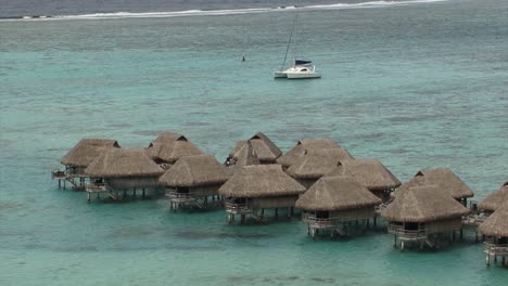 Overwater-wooden-houses-and-a-yacht-in-the-blue-lagoon-in-Moorea,-French-Polynesia