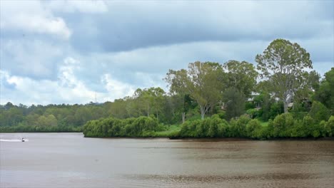 A-speeding-jetski-flies-from-left-to-right,-in-this-beautiful-Australian-river-scene-in-the-Queensland-rainforest