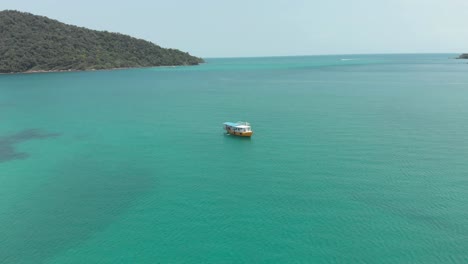 Lone-Cambodian-Boat-in-the-middle-of-the-turquoise-paradisiac-sea-in-M'pai-Bay,-Koh-Rong-Sanloem,-Cambodia---Aerial-Top-view-Fly-over