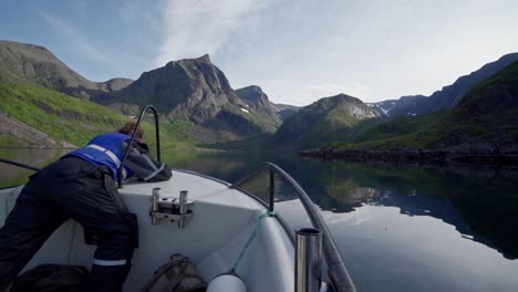 Mann-Am-Bug-Eines-Bootes,-Das-Tagsüber-In-Norwegen-Auf-Einem-Kristallklaren-See-Durch-Felsige-Berge-Schwimmt