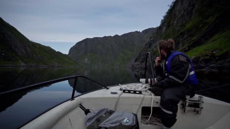 Norwegian-Seated-On-The-Front-Edge-Of-His-Boat-While-Sailing-In-Peaceful-Lake-Of-Norway