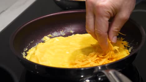Hinzufügen-Von-Geriebenem-Cheddar-Käse-Zu-Ei-Omelett-In-Der-Pfanne---Kochen-In-Der-Küche