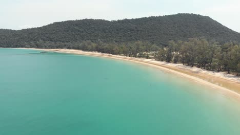 Golden-sand-beach-sidelining-the-clean-crystal-turquoise-water-of-M'pai-Bay,-in-Koh-Rong-Sanloem-Island,-Cambodia---Aerial-Fly-over-shot