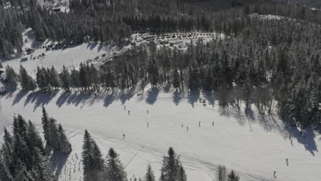 Ribnica-Track-at-Kope-ski-resort-Slovenia-with-skiers-going-downhill,-Aerial-pan-left-reveal-shot