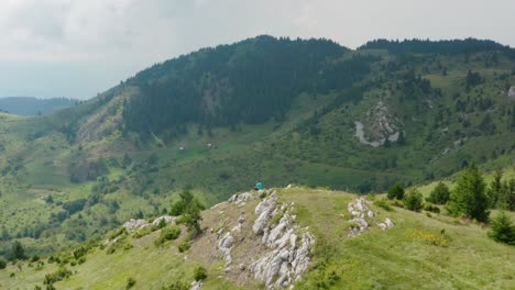 Stunning-Mountain-Scenery-Of-Jadovnik-In-Serbia---Male-Hiker-Sitting-On-Top-Of-The-Rocky-Peak-Overlooking-Mountain-Landscape---aerial-drone-shot