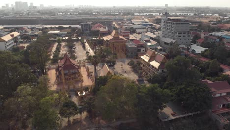 Vista-Desde-La-Orilla-Del-Río-Mekong-Hasta-El-Templo-Dorado-De-Phnom-Penh-En-Medio-Del-Paisaje-Urbano---Tiro-Aéreo-Amplio-Sobrevuelo