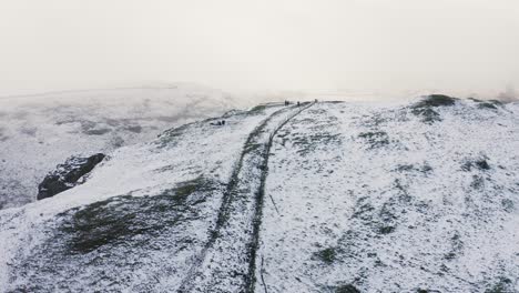 Aerial-footage-of-hikers-walking-up-a-snow-capped-mountain-in-the-Peak-District