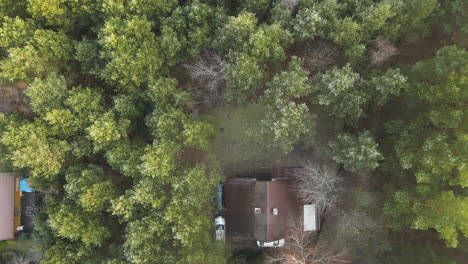 Drone-truck-shot-from-above-the-green-forest-on-a-house-between-the-trees-in-Bartoszylas,-Poland-on-a-cloudy-day