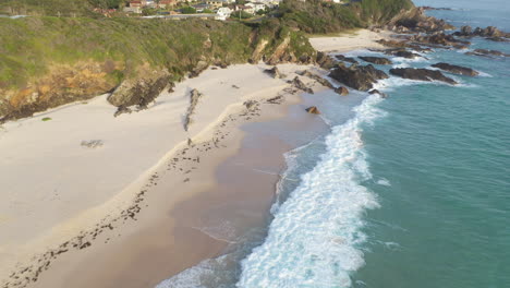 Waves-sea-level-retracing-from-rocky-Australian-beach,-backwards-aerial-reveal