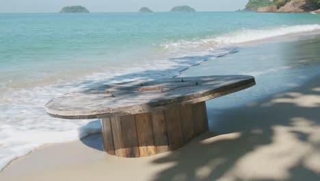 Deserted-beach-in-Thailand-with-cable-wheel-in-sand-with-waves-lapping