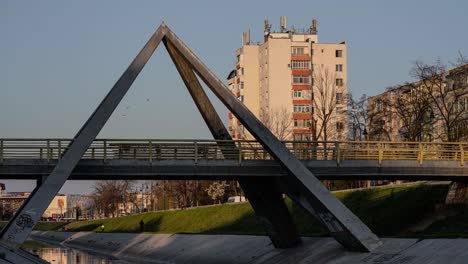 Sunset-timelapse-showing-an-urban-landscape,-people-crossing-a-triangle-bridge-and-birds-movement