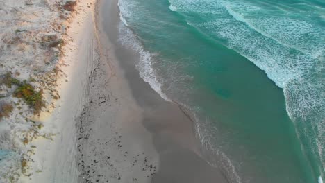 Turquoise-ocean-water-and-empty-white-sand-beach-aerial-view,-golden-sunlight