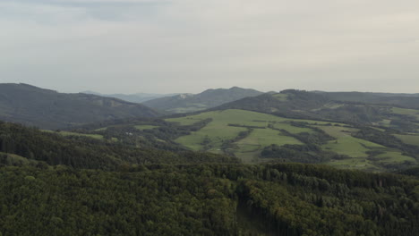 Sideways-aerial-shot-of-hilly-green-forests-and-fields,-Czech-Republic