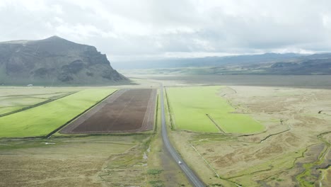 Vast-Icelandic-landscape-with-long-road-in-different-weather-conditions,-aerial