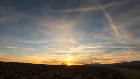 Golden-sunset-and-colorful,-dynamic-cloudscape-over-the-arid-terrain-of-the-Mojave-Desert---wide-angle-time-lapse