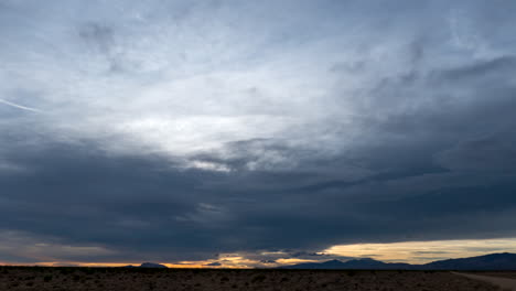 Clouds-cross-the-sky-as-the-sun-sets-beyond-the-distant-mountains-in-the-Mojave-Desert---wide-angle-static-time-lapse