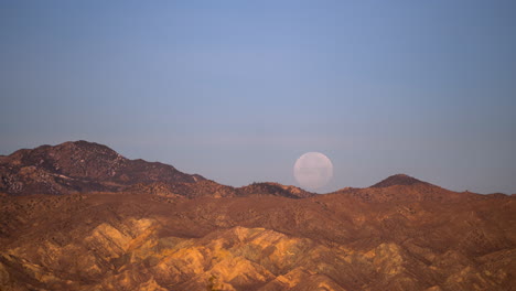 The-full-moon-sets-behind-the-rugged-terrain-in-the-Mojave-Desert---time-lapse