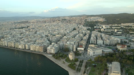 Filmische-Breite-Drohnenluftaufnahme-Der-Nordgriechischen-Stadt-Thessaloniki-Mit-Dem-Meer-Und-Der-Stadt-Und-Dem-Weißen-Turm-Im-Blick-Bei-Sonnenuntergang,-Die-Sich-In-4k-Rückwärts-Bewegt