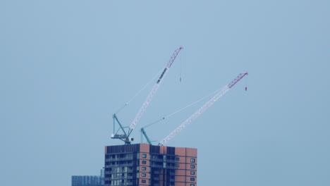 Distant-View-Of-Tower-Cranes-With-Warning-Lights-Blinking-Against-Clear-Sky-Background,-static,-slow-motion