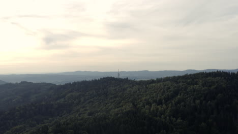Wide-rising-aerial-of-hilly-forest-and-distant-town-in-Central-Europe