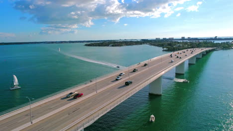 Following-vehicle-traffic-over-a-water-bridge-in-a-tropical-setting-while-boats-pass-underneath-bridge