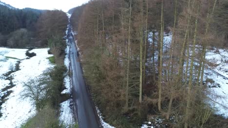 Snowy-Welsh-woodland-Moel-Famau-winter-landscape-aerial-view-descending-right-across-rural-road
