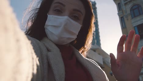 Slow-Motion:Beautiful-girl-wearing-protective-disposable-medical-mask-and-fashionable-clothes-waves-her-hand-while-taking-selfie-with-smartphone