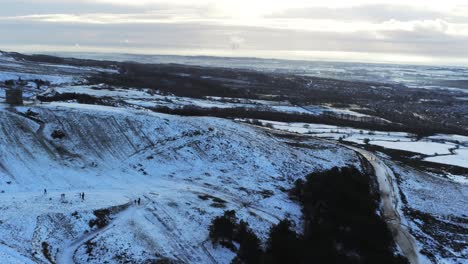 Snowy-Rivington-Pike-tower-Winter-hill-aerial-slow-pan-right-view-people-sledding-downhill-at-sunrise