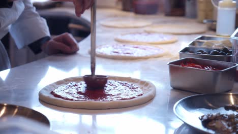 Küchenchef-Fügt-Tomatensauce-Auf-Pizza-Neapolitana-Auf-Dem-Küchentisch-Hinzu