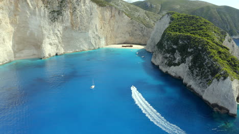 A-boat-tour-approaching-Naviago-beach-from-a-drone-aerial-shot-in-Zakynthos,-Greece