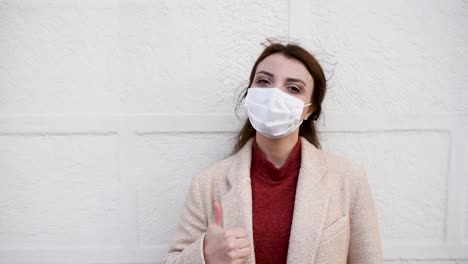 Beautiful-girl-wearing-protective-medical-mask-and-fashionable-clothes-does-thumbs-up-gesture