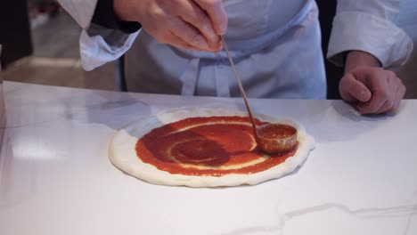 Chef-adds-tomato-sauce-on-top-of-pizza-Neapolitana-on-the-kitchen-table