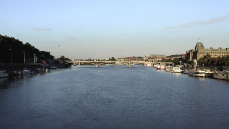 Vltava-river-in-Prague,Czechia,with-anchored-boats-on-each-side,bridge