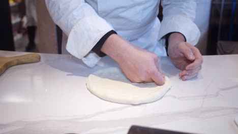 Chef-forming-the-pizza-dough-on-the-kitchen-table-in-the-restaurant
