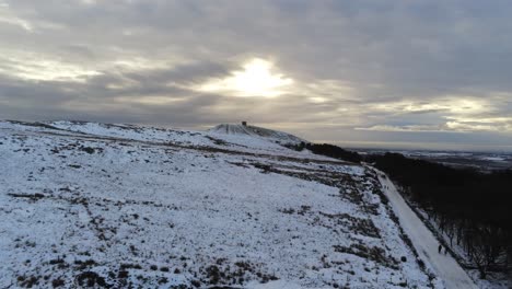 Snowy-Rivington-Pike-tower-Winter-hill-aerial-view-people-sledding-downhill-at-sunrise-rising