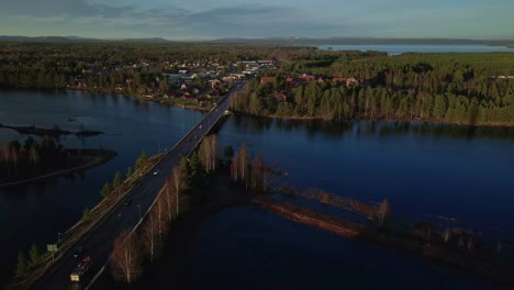 Cars-Driving-on-a-Bridge-in-Small-Town-Mora,-Vast-Fir-Forest,-Aerial